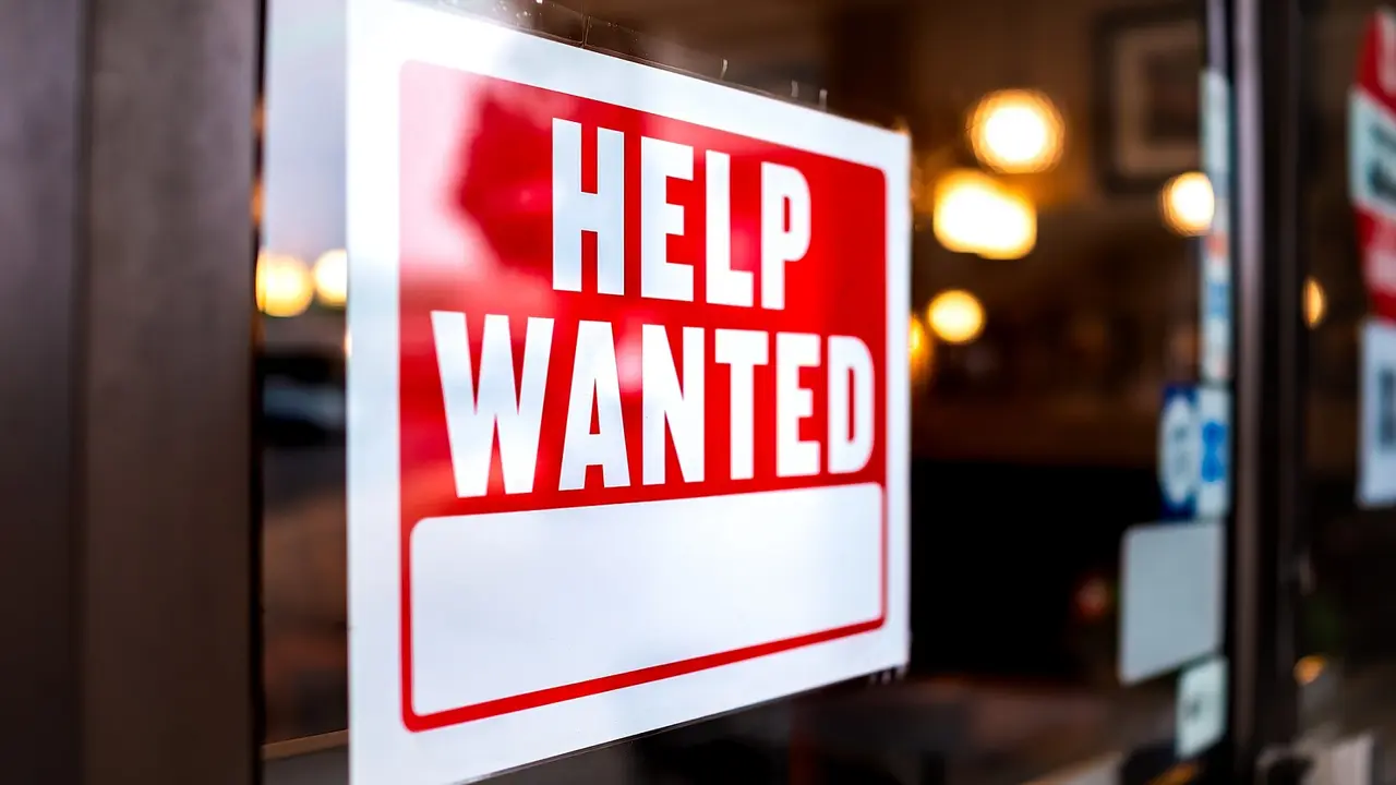 Sign text closeup for help wanted with red and white colors by entrance to store shop business building during corona virus covid 19 pandemic stock photo
