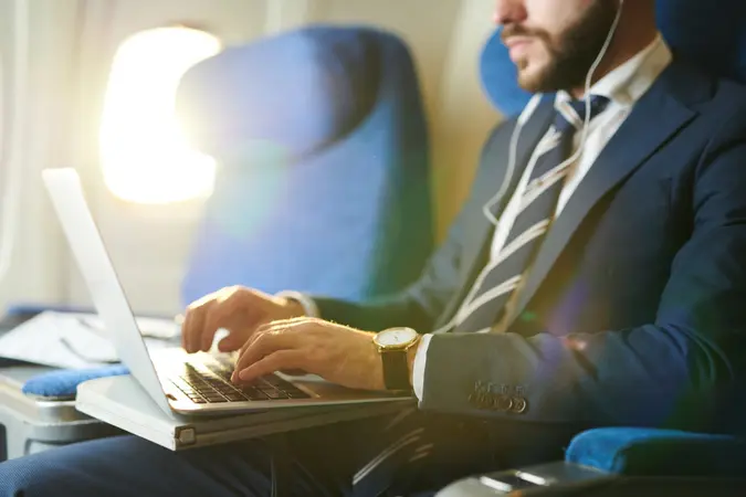 Mid section portrait of unrecognizable businessman typing on keyboard while using laptop during first class flight in plane, copy space.