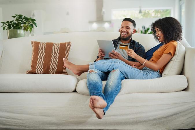 Shot of a young couple using a digital tablet and credit card while relaxing at home.