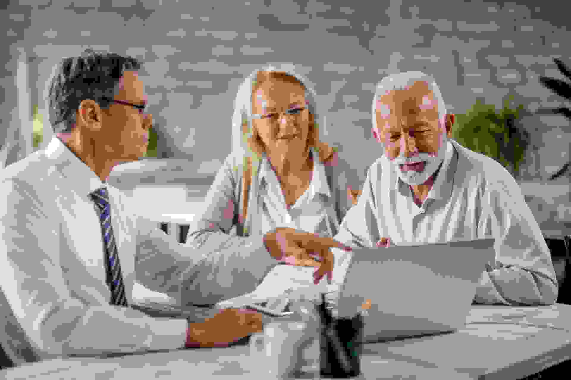 Senior couple using laptop with their financial advisor during a meeting int he office.