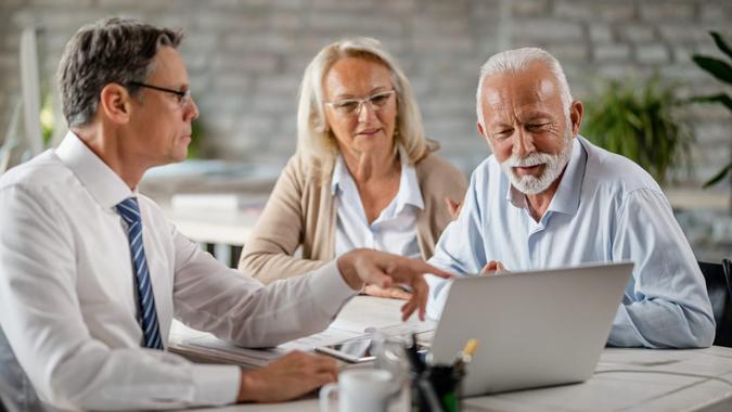 Senior couple using laptop with their financial advisor during a meeting int he office.