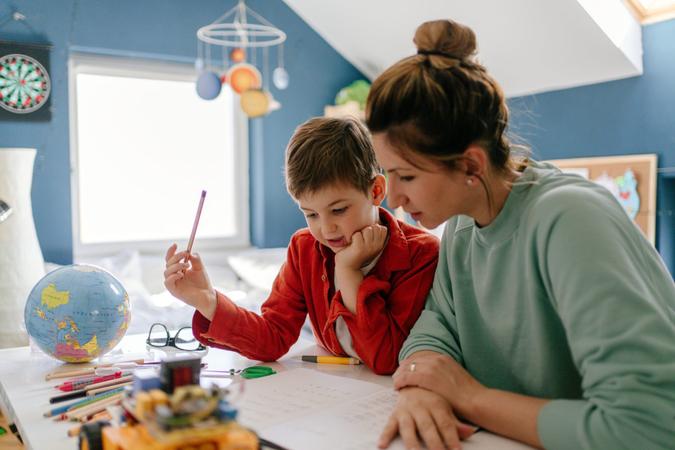 Photo of a young boy being homeschooled by his mother in his bedroom.