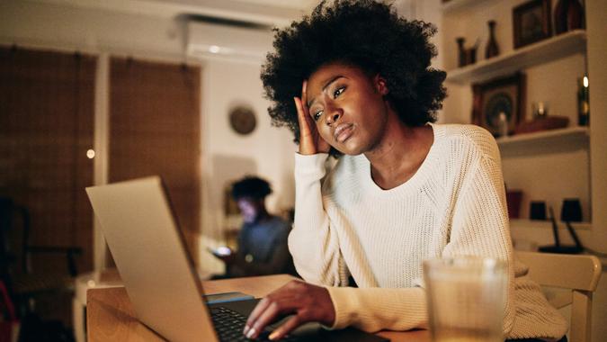 Worn out African American woman doing freelance work on a laptop and struggling with a problem.