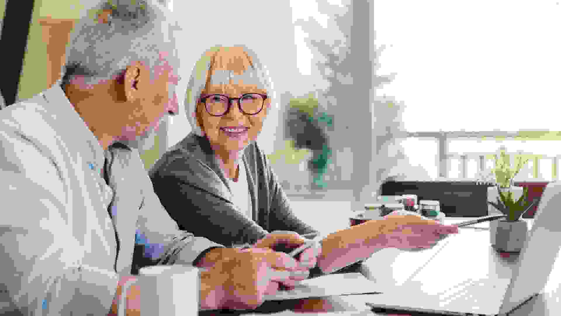 Senior couple doing home finances using laptop indoors.