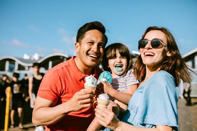 A portrait of a father, mother, and daughter enjoying ice cream cones at the Santa Monica Pier in Los Angeles, California.