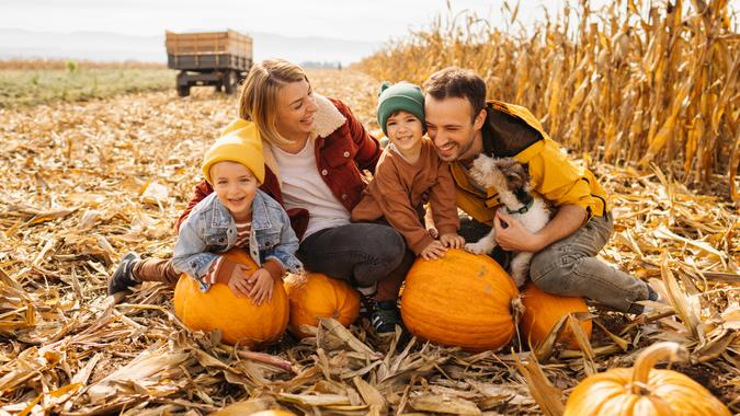 Photo of a happy young family and their dog enjoying their autumn days on a pumpkin field; family exploring pumpkin patches in the fall and preparing for the upcoming holidays.