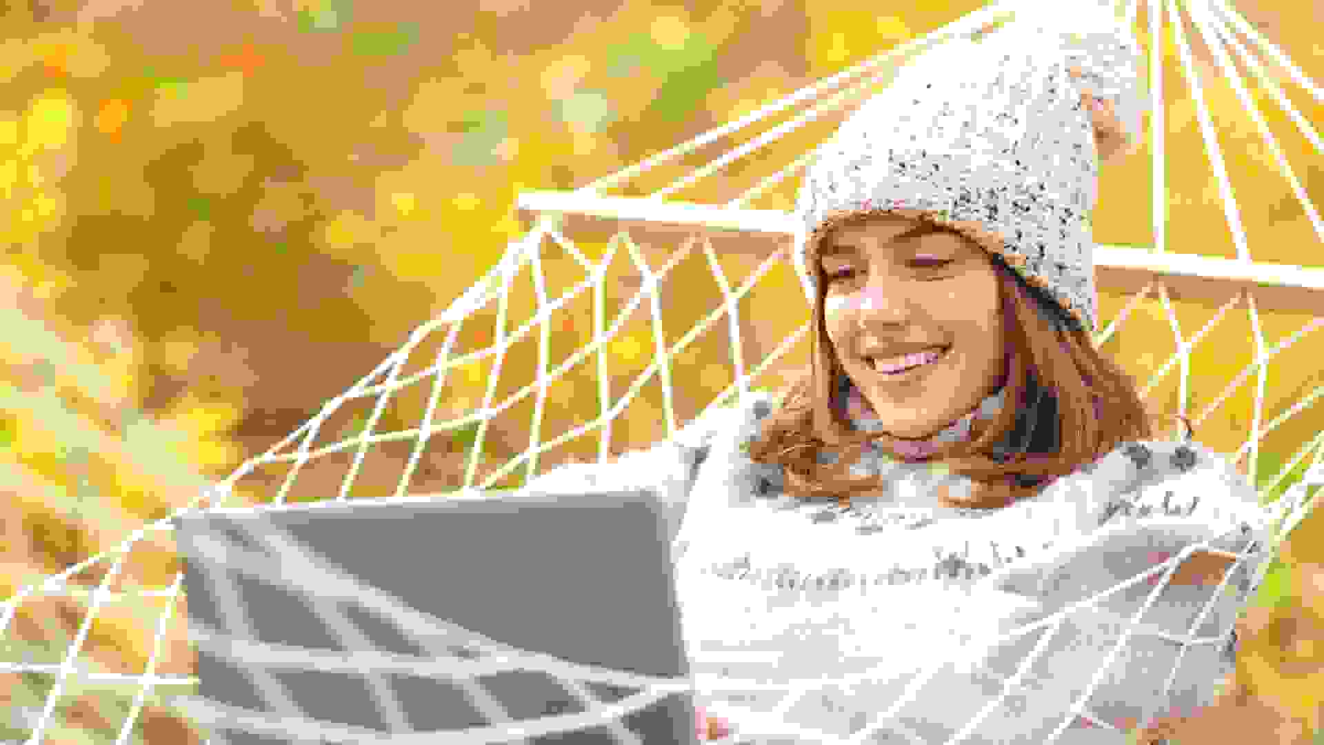 Happy woman on hammock using laptop in autumn.