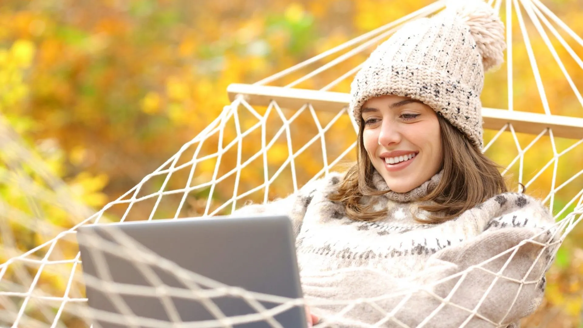在秋天快乐的女人在吊床上使用笔记本电脑。