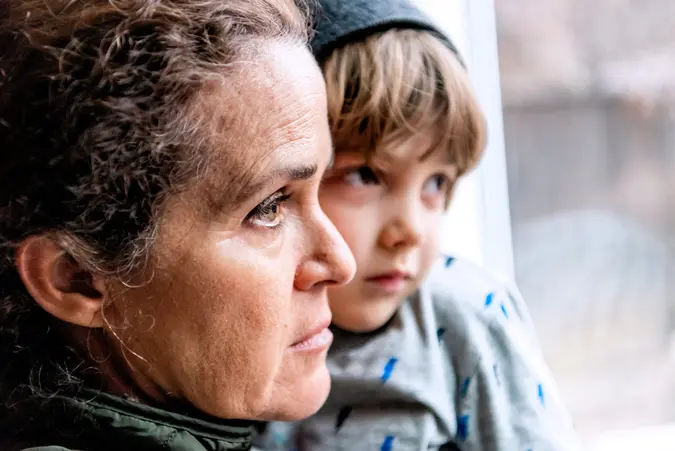 Caucasian Mature woman posing with her son, very sad looking through window worried about loss of her job due Covid-19 pandemic.