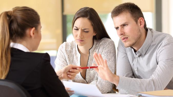 Saleswoman offering a pen to a couple of angry customers that rejects to sing a contract at office.