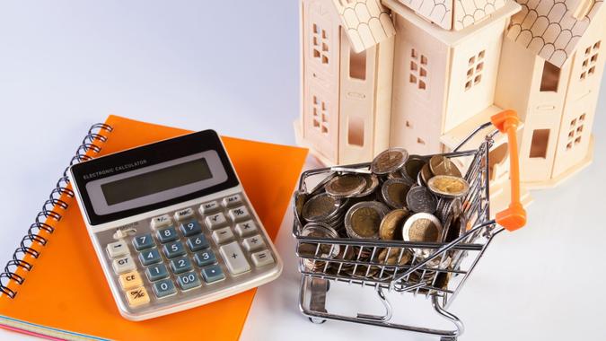 Wood house model, coins in shopping cart and financial notebook on desk table.