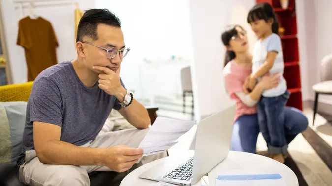 Worried man calculating bills while wife and daughter playing stock photo