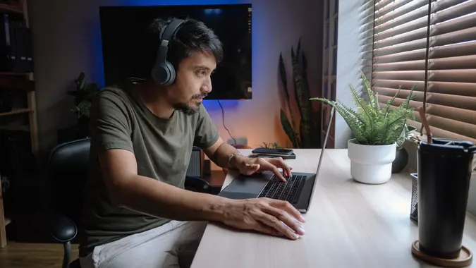 Millennial man playing computer game on laptop at home. stock photo