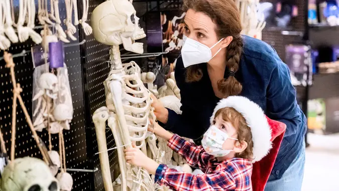 Mother and son shopping for halloween skulls in a store wearing protective face masks stock photo