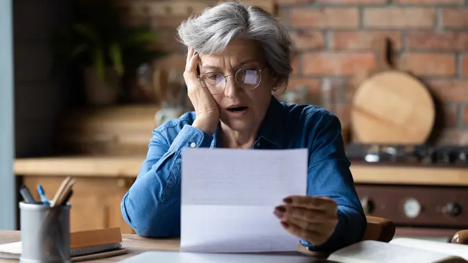 Unhappy mature woman reading bad news in letter.