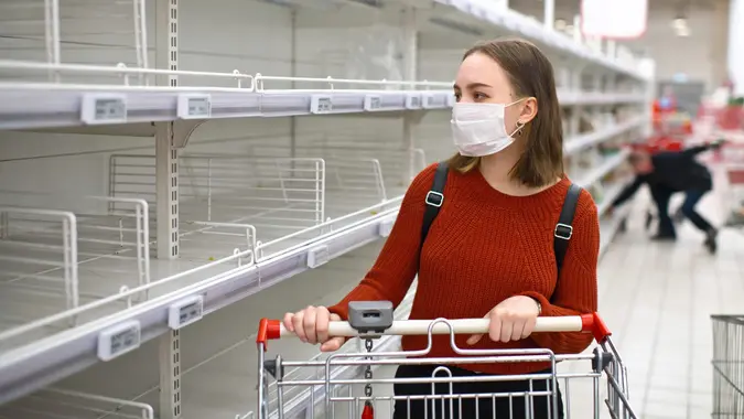 Young woman standing in front of empty shelf in a supermarket stock photo