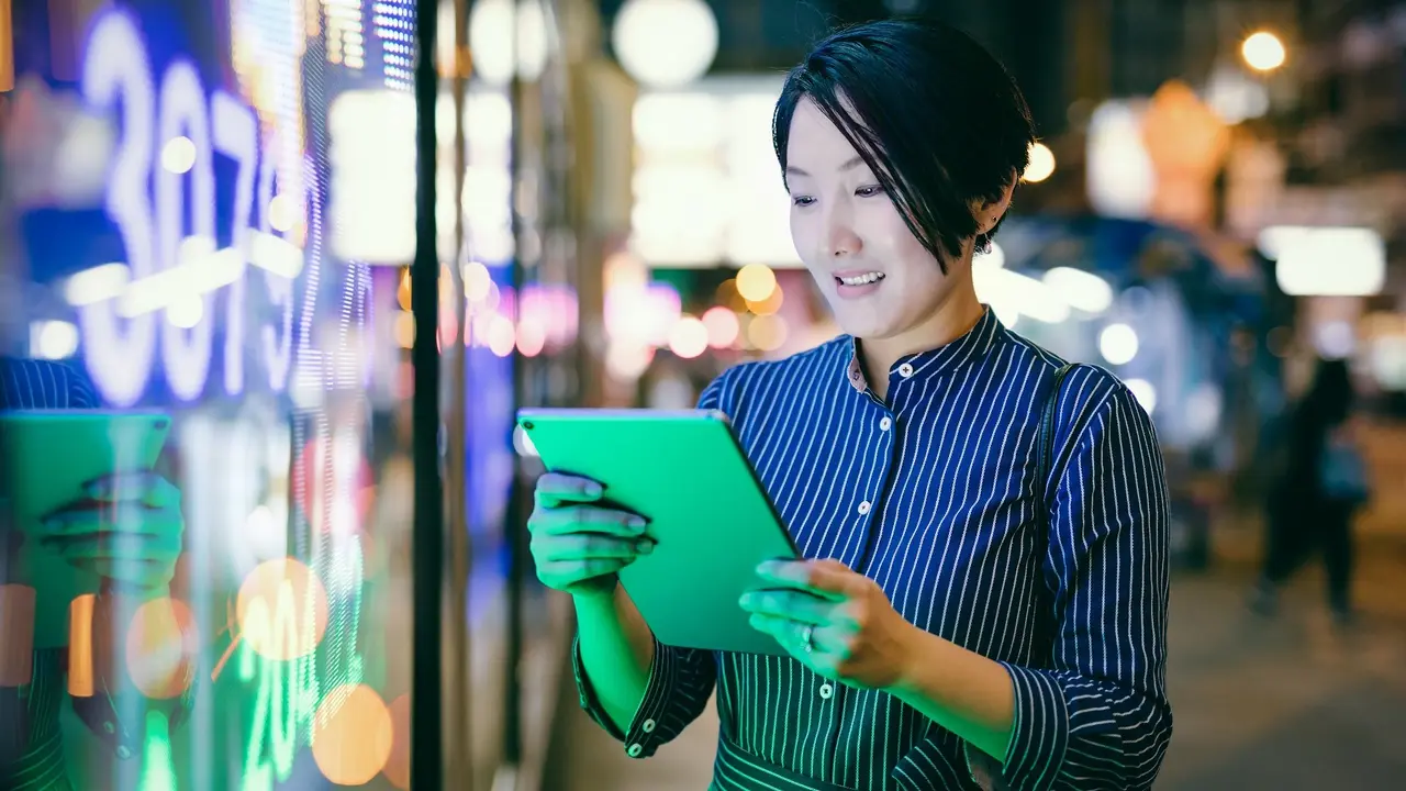 Asian businesswomen checking stock market data on tablet before Hong Kong financial display board stock photo