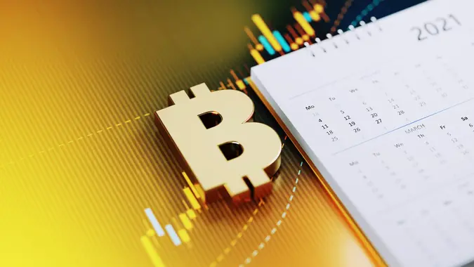 Investment And Financial Planning Concept - Bitcoin Symbol Sitting Next To The White 2021 Calendar On Yellow Financial Graph Background stock photo
