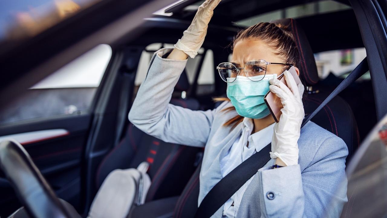 Businesswoman with protective mask and gloves on sitting in her car caught in traffic jam sitting in her car and having phone conversation. She is very nervous. Protection form corona virus concept. stock photo