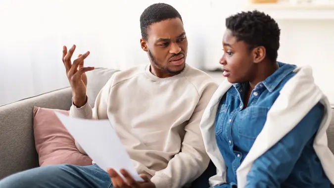 Confused afro couple reading documentation at home, sitting on sofa stock photo