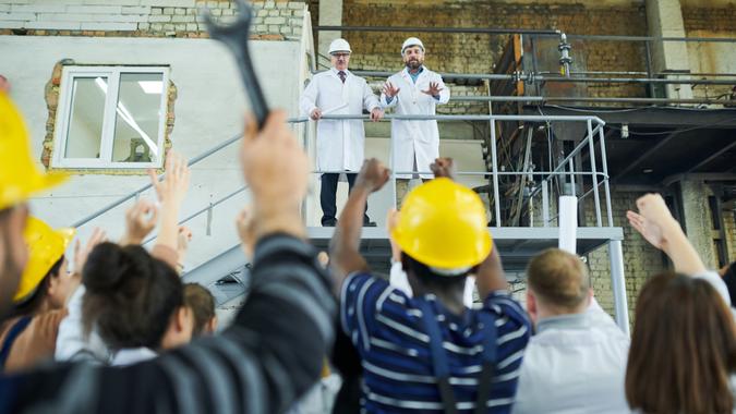 Rear view portrait of multi-ethnic group of workers protesting looking at two factory managers standing at balcony, copy space.