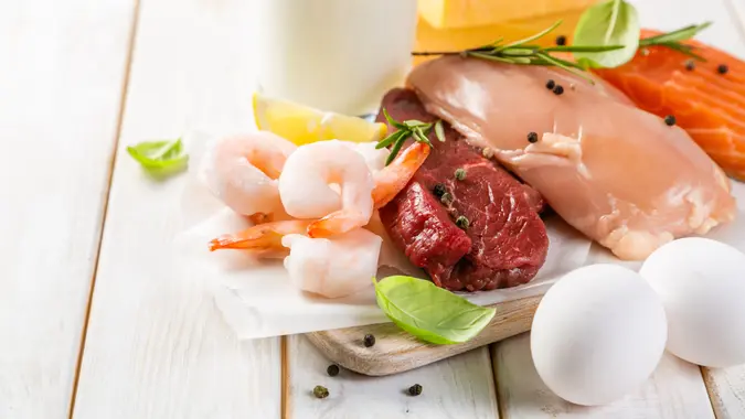 Selection of aminal protein sources - beef, chicken, salmon, cheese, milk, eggs, shrimps on wood background.