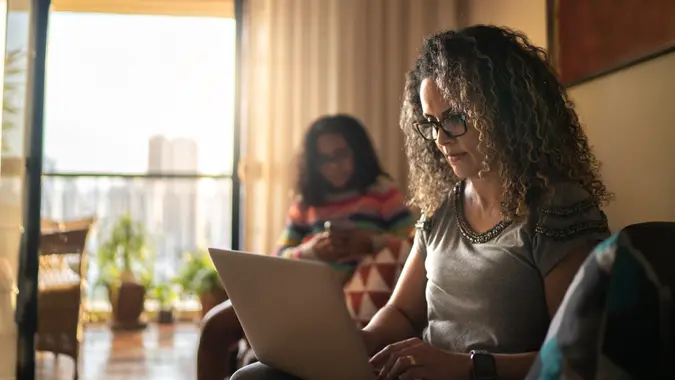 Mature woman working at home, using laptop sitting on the couch.