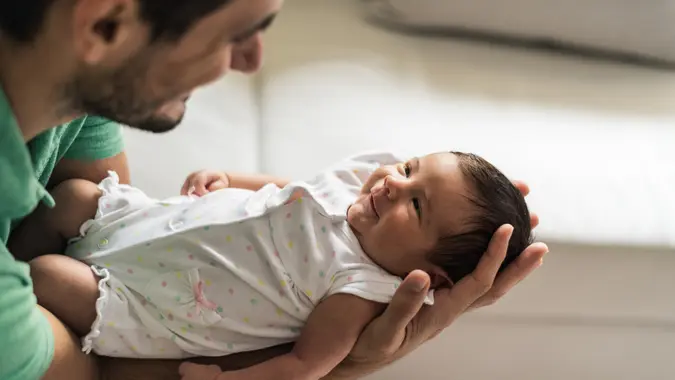 Young father is embracing newborn baby.