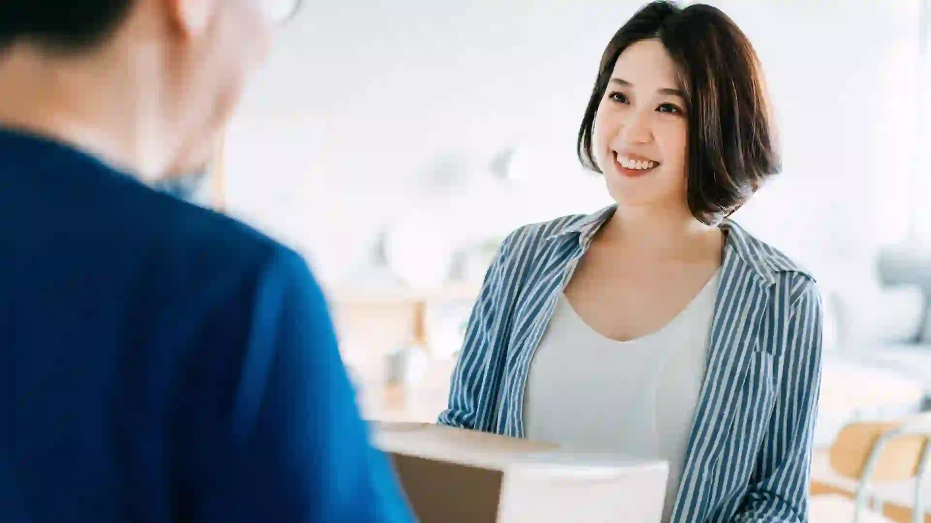 Cheerful young Asian woman receiving her parcel from a delivery man at home.