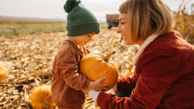 Photo of a young mother and her son collecting pumpkins on a pumpkin patch; family on a Halloween pumpkin patch adventure.