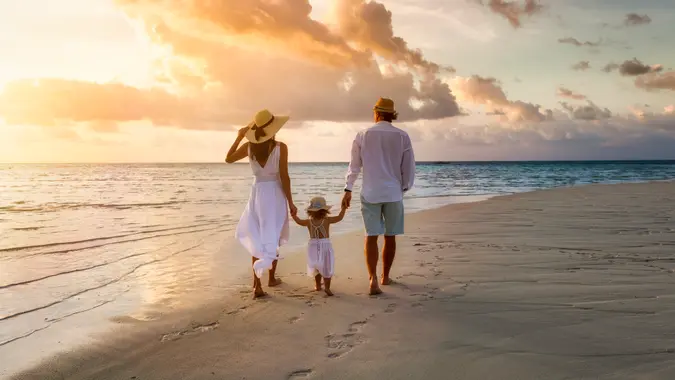 A elegant family in white summer clothing walks hand in hand down a tropical paradise beach during sunset tme and enjoys their vacation time.