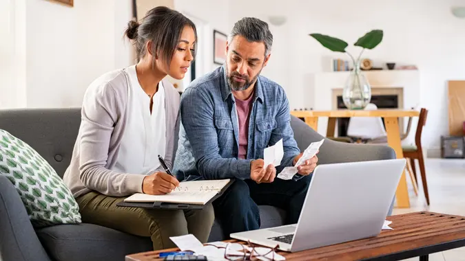 Mature couple calculating bills at home using laptop and calculator.