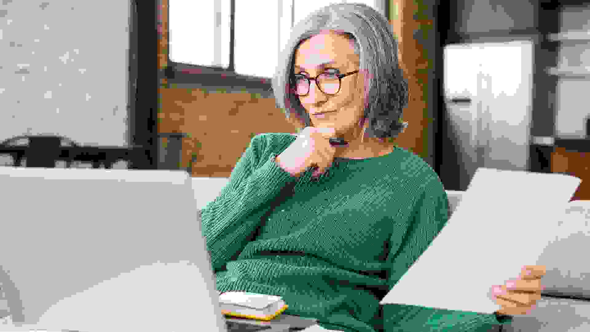 Serious senior accountant sitting on the living room and looking at the laptop stock photo