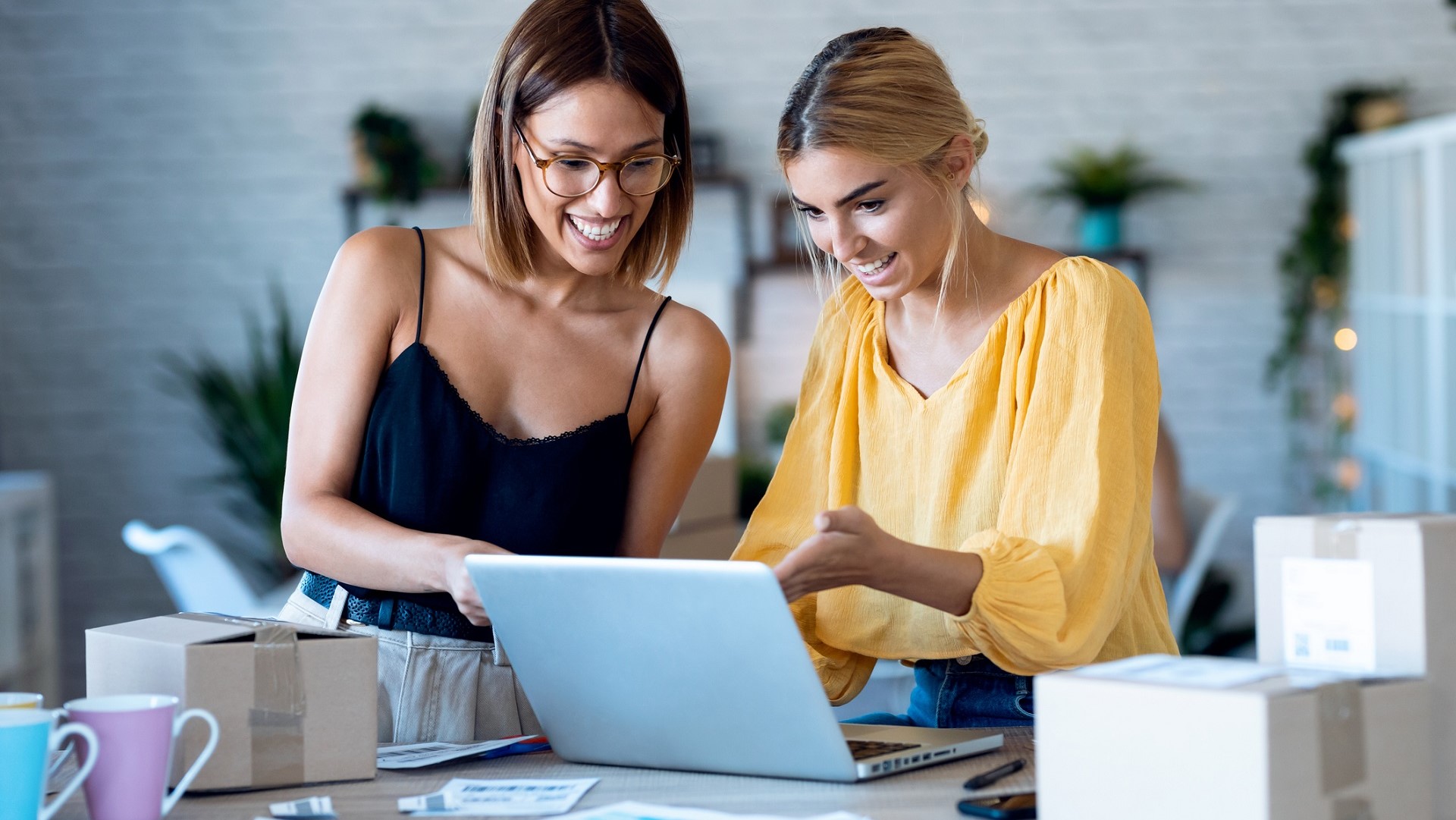 two young female entrepreneurs small business owners check online orders pack boxes iStock 1277440304.