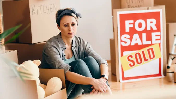 Sad woman sitting among her belongings after selling her home. stock photo
