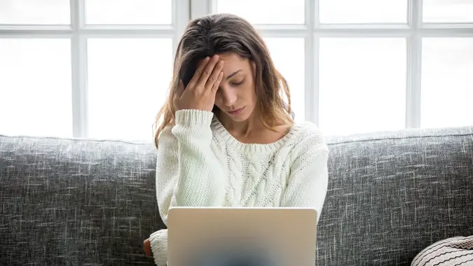 Frustrated woman worried about problem sitting on sofa with laptop stock photo