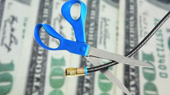 blue scissors cut coax cable cord with 100 dollar bill background_iStock-476992998 Cable cut over money stock photo