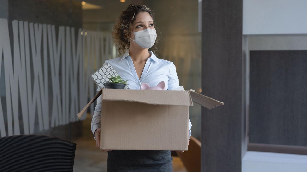 Worker wearing a facemask at the office while holding a box with her belongings after being fired stock photo