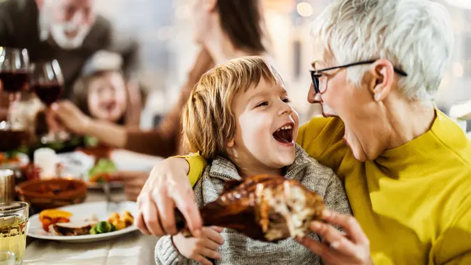Happy boy and his grandmother about to eat turkey leg at dining table. stock photo