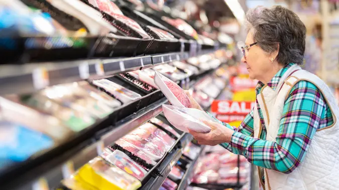 Senior woman comparing prices for meat selection.