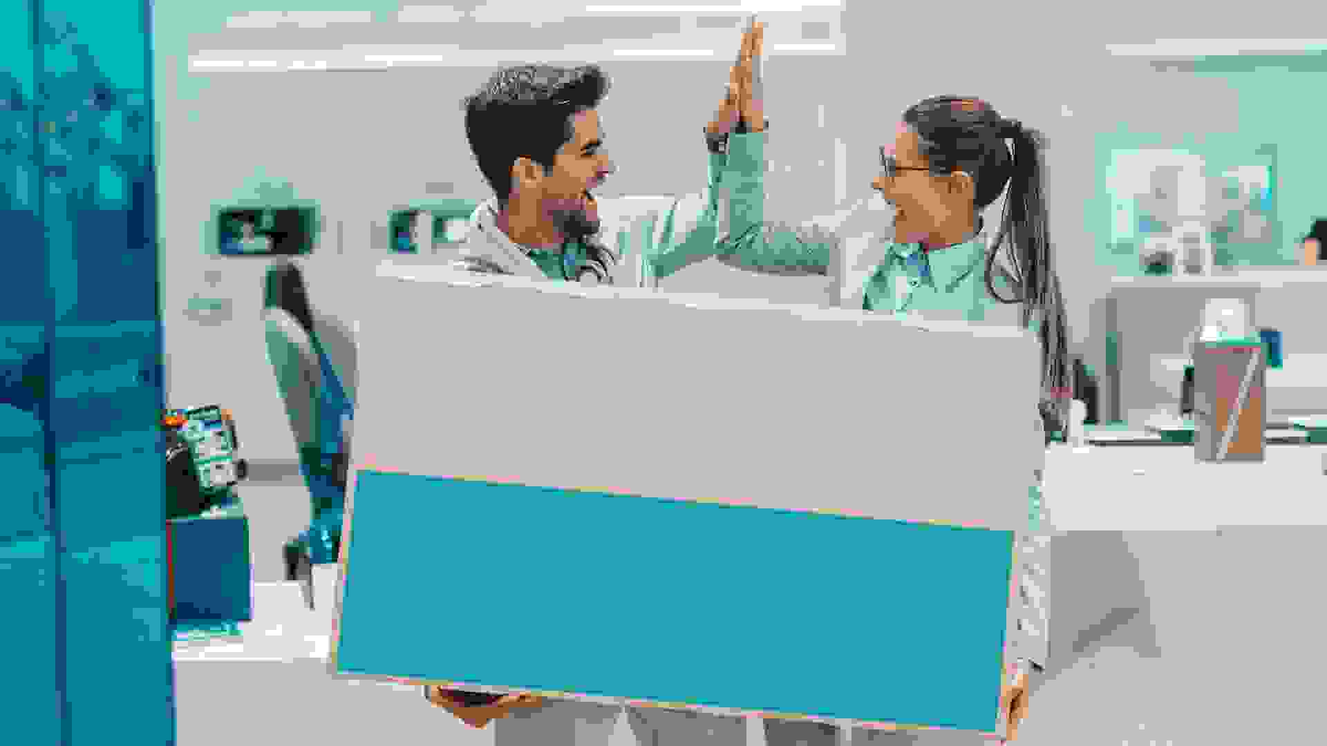 Smiling happy multicultural couple dressed elegant holding box with new plasma tv and giving high five to each other while standing in tech store.