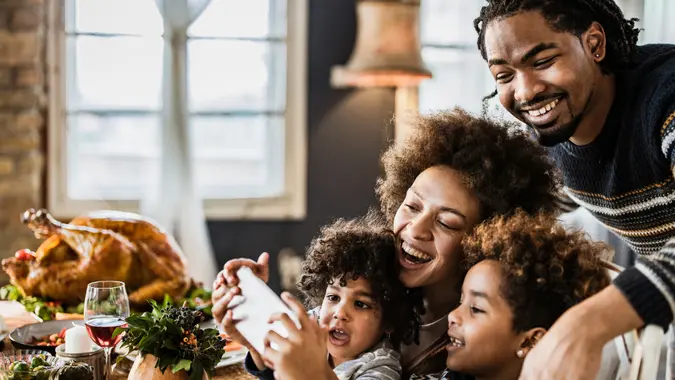 Happy black family having fun while taking a selfie on Thanksgiving lunch at dining table.
