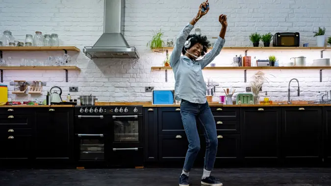 Very happy African American woman having fun listening to music at home and dancing in the kitchen.