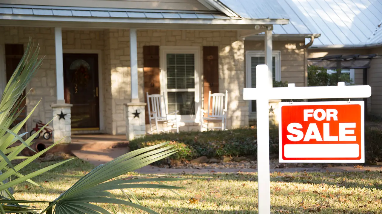 Home for sale with red and white real estate sign during the fall season.
