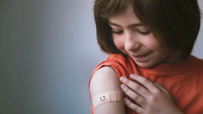 Portrait of a smiling little child with adhesive bandage on his hand after COVID-19 vaccine.