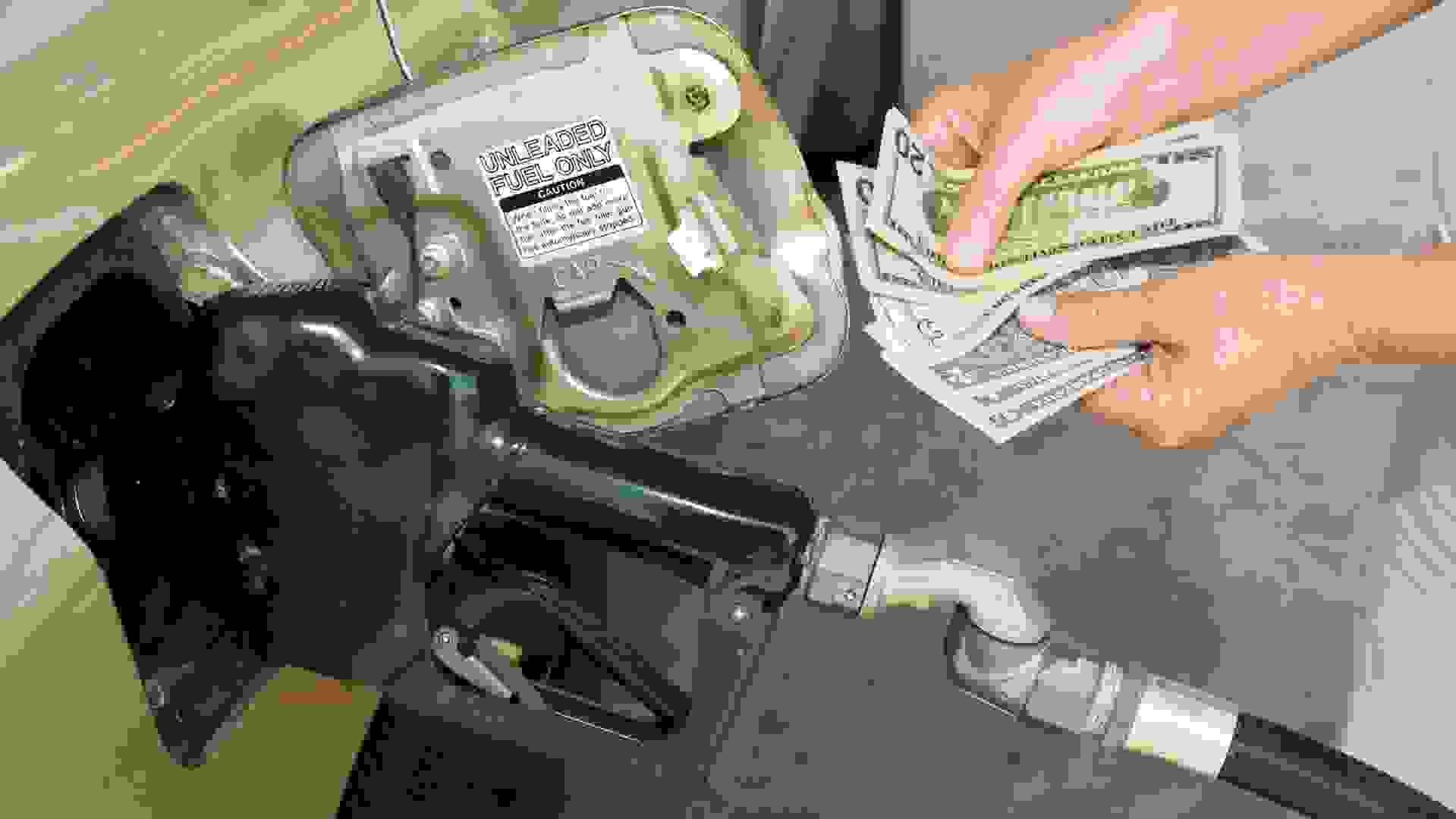 Horizontal shot of someone's hands holding money at the gas pump.