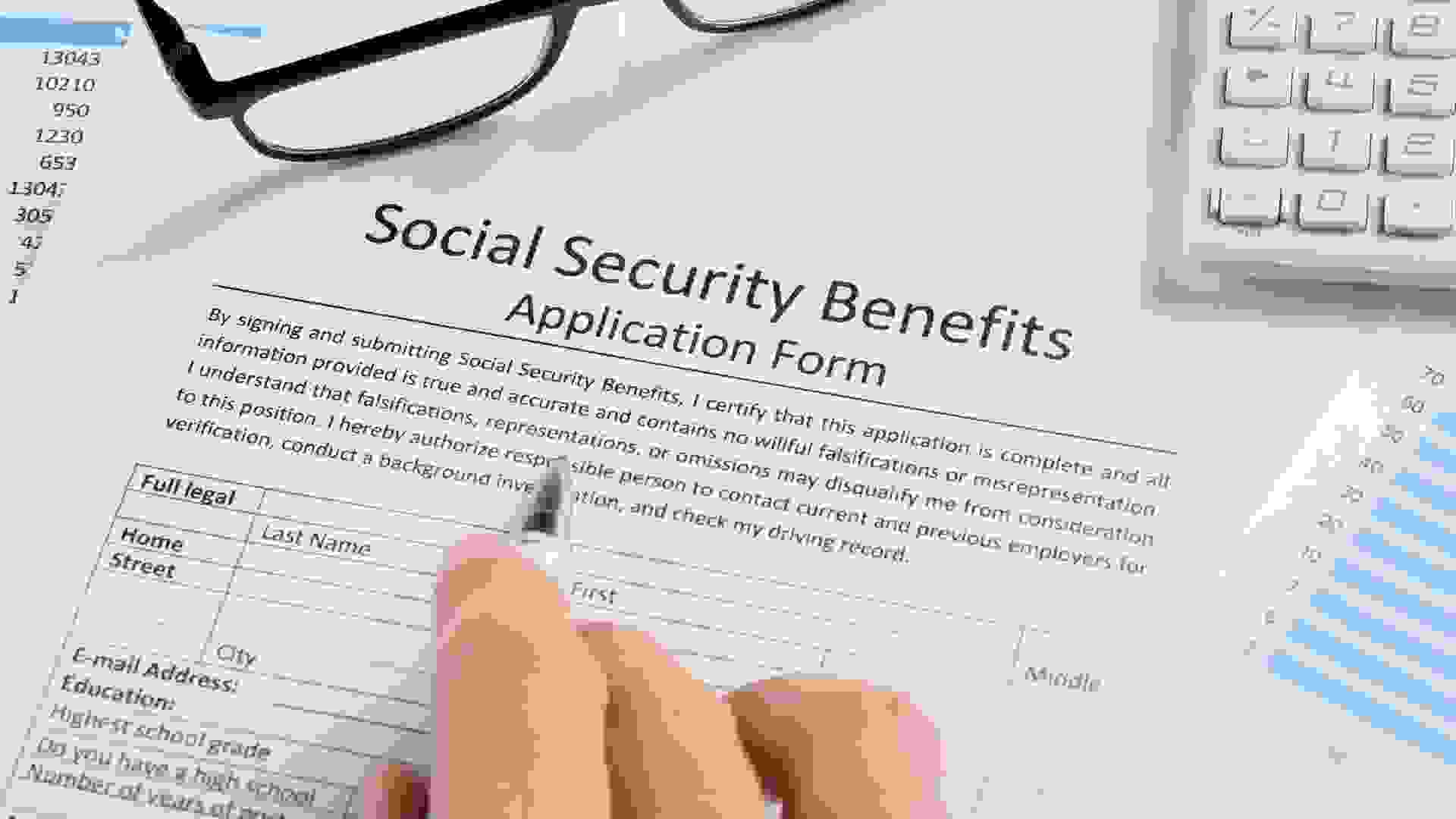 Close-up Of Hand With Pen And Eyeglasses Over Social Security Benefits Application Form.