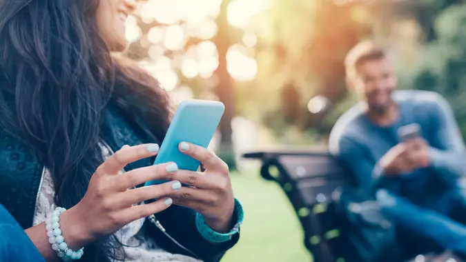 Flirting couple in the park texting on smartphones stock photo