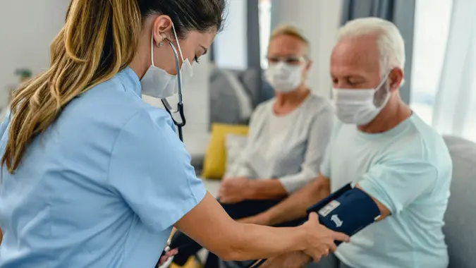 Nurse measuring blood pressure of senior man at checkup meeting at home stock photo