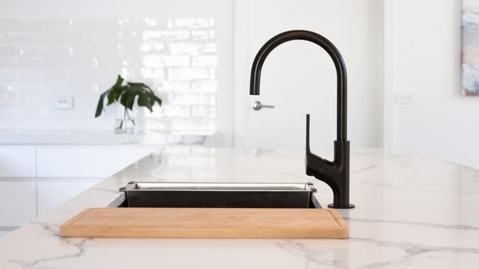 Monochrome kitchen detail of black gooseneck tap set in a white marble counter top.